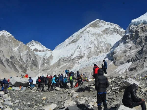 Trekkers at Everest Base Camp with Khumbu Icefall and prayer flags