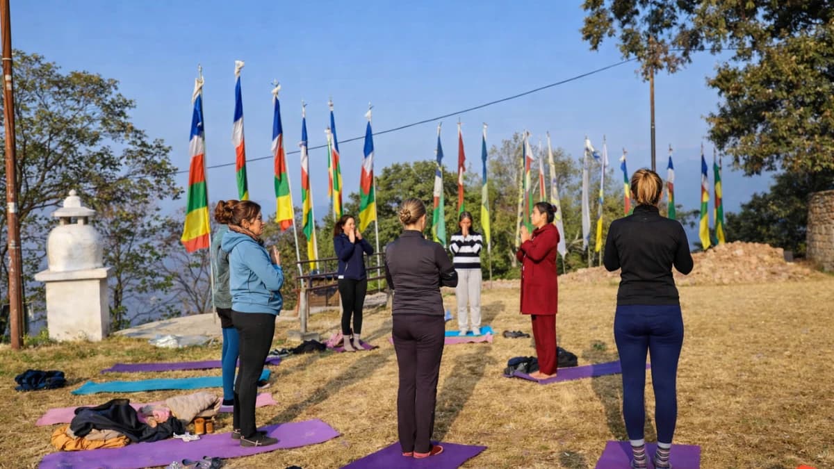 People practicing yoga outdoors on a hillside with colorful prayer flags in the background.