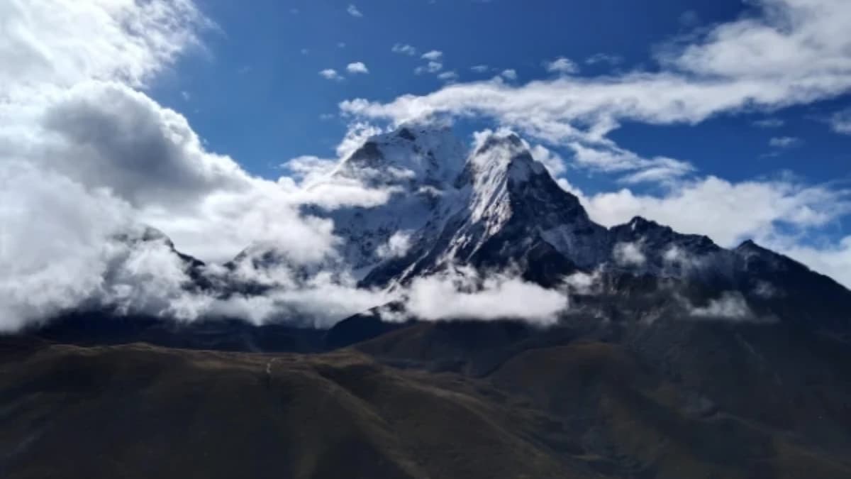 Tall rocky mountain with white snow patches and moving clouds across the summit.
